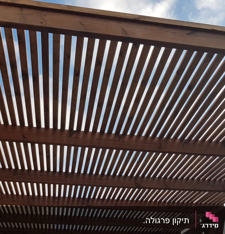 פרגולה מעץ עם קורות אופקיות בשמיים בהירים